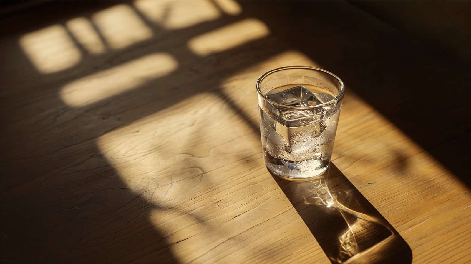 a neat glass of vodka on a wooden table in window sunlight